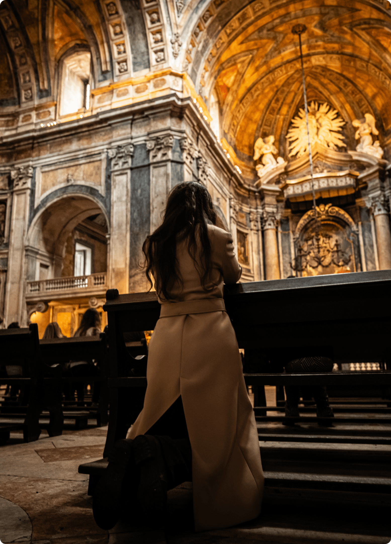 Person kneeling in ornate church interior.