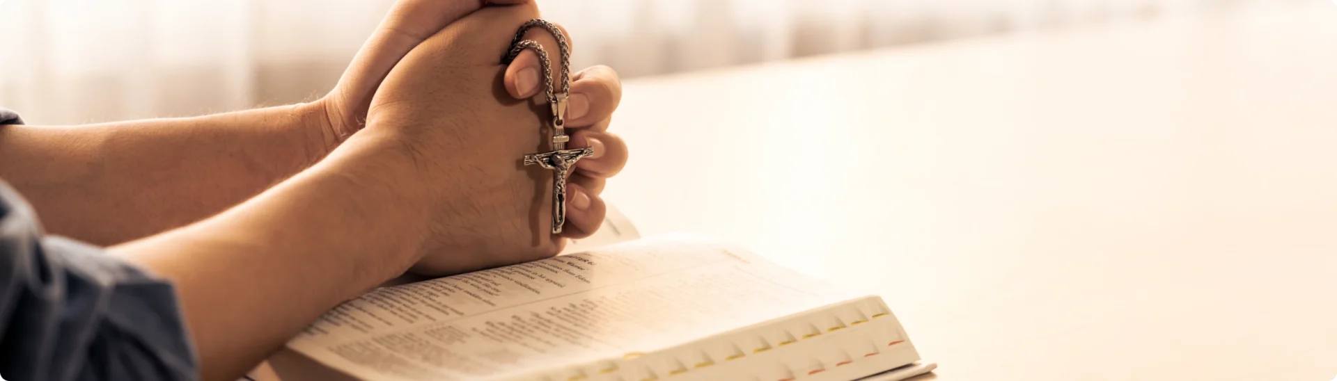 Hands holding rosary over open book.